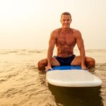 Surfer fitness male with a muscular body with his surfboard at the beach warm up.